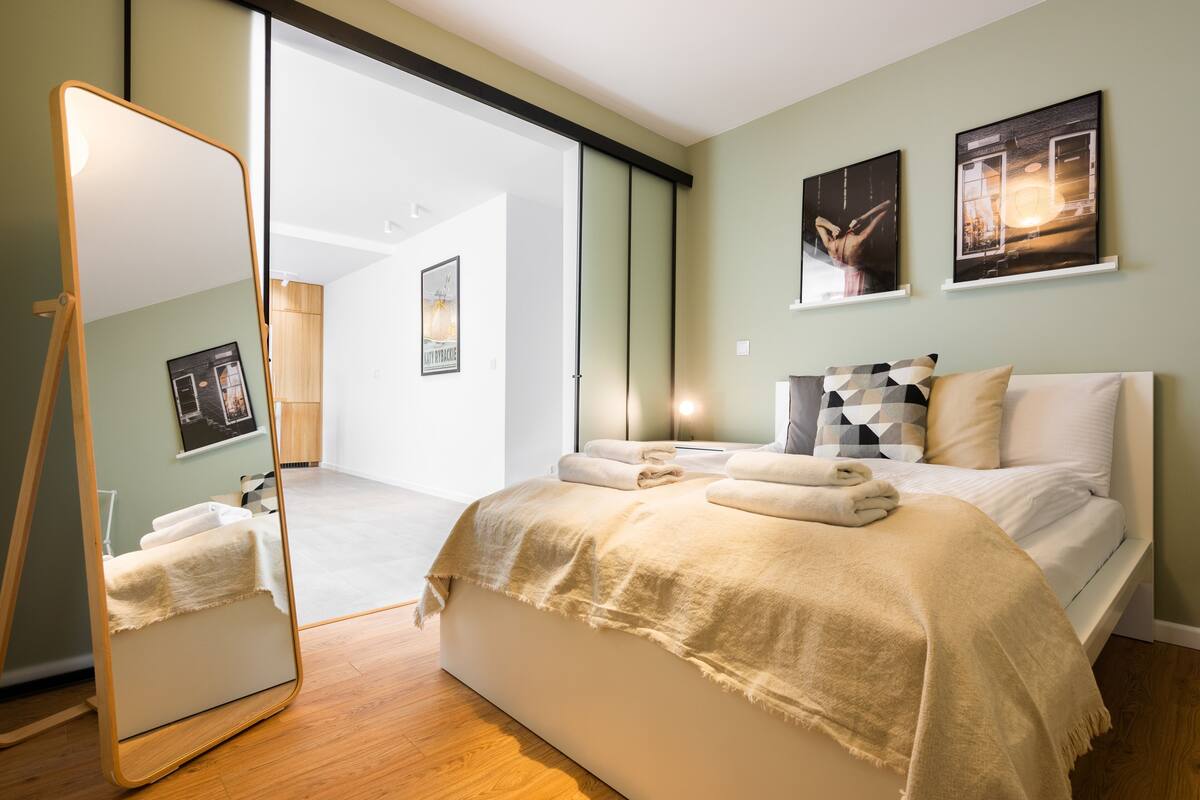 A modern bedroom with a large bed, a bedside mirror, and artwork on the walls.