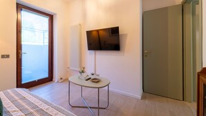 Un dormitorio moderno con cama, una mesita, un televisor y una puerta corrediza de vidrio.