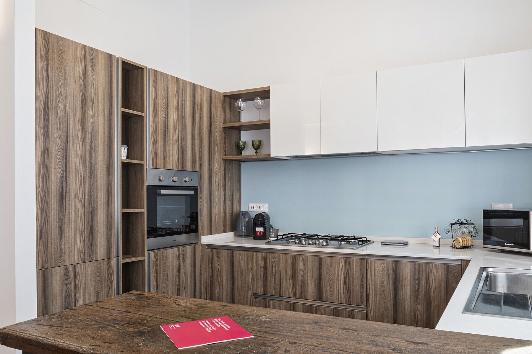 A modern kitchen with wooden cabinetry, a built-in oven, a gas stove, and a coffee machine.