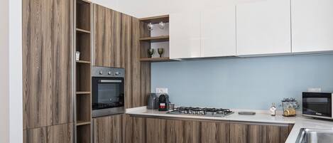 A modern kitchen with wooden cabinetry, a built-in oven, a gas stove, and a coffee machine.