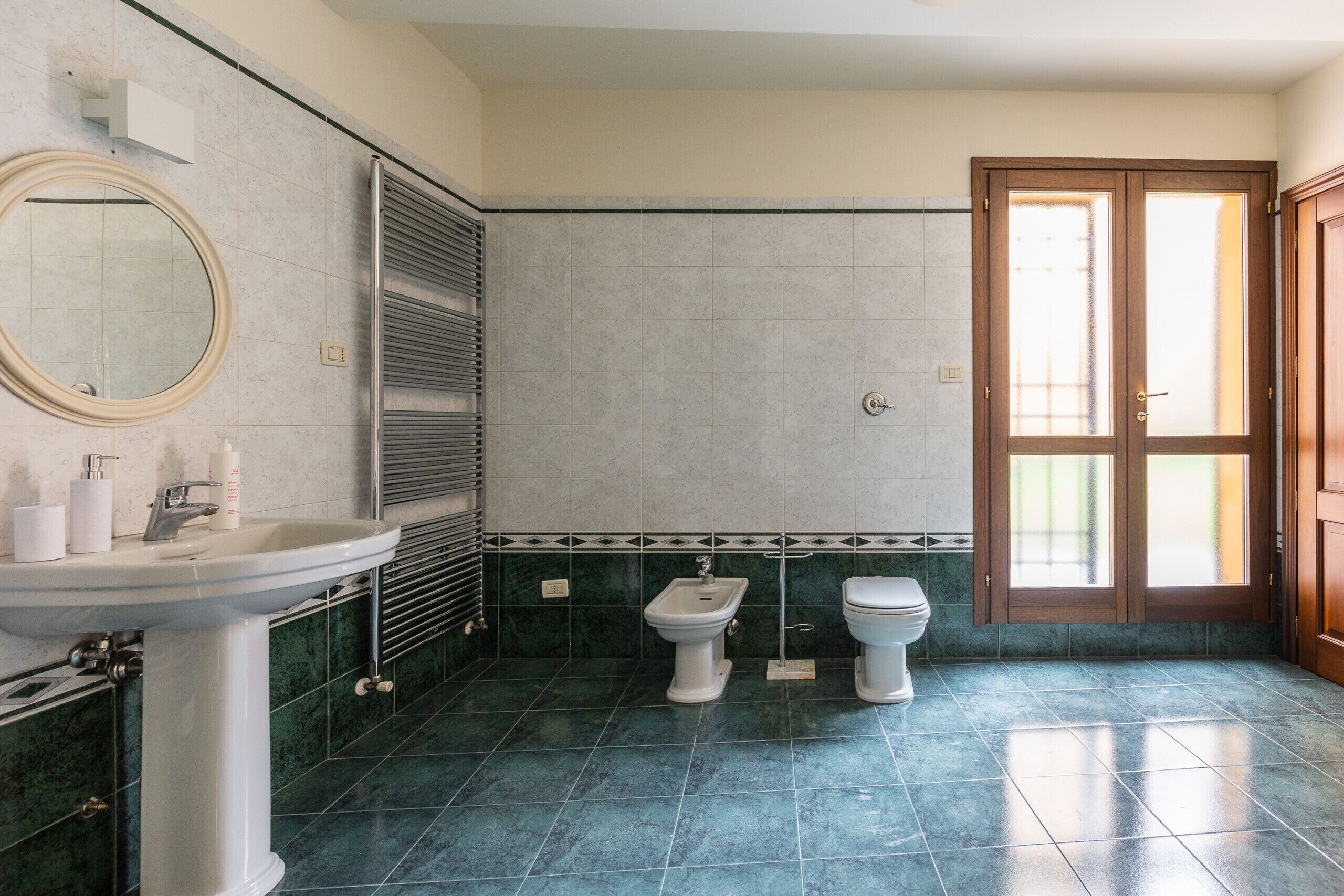 Een badkamer met een wastafel, spiegel, toilet, wc en een deur naar een andere ruimte.