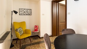 A hotel room with a yellow armchair, a small table with a red box, a floor lamp, and a large wooden door.