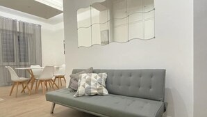 A modern living room with a grey sofa, a dining table with chairs, and a large mirror on the wall. - Home Vatican Oasis (Roma)