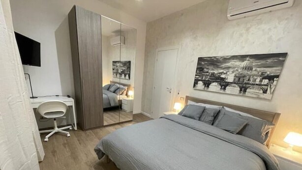 A bedroom with a bed, bedside tables, a desk, a chair, a wardrobe, a mirror, and a wall-mounted air conditioner. - Home Vatican Oasis (Roma)