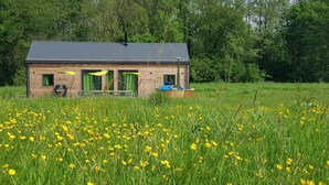 Une cabane en bois, surmontée d’un toit en métal, entourée d’un champ de fleurs jaunes.