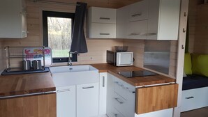 Une cuisine de taille réduite avec des meubles blancs, un plan de travail en bois, un évier, un four à micro-ondes et une fenêtre donnant sur les arbres.