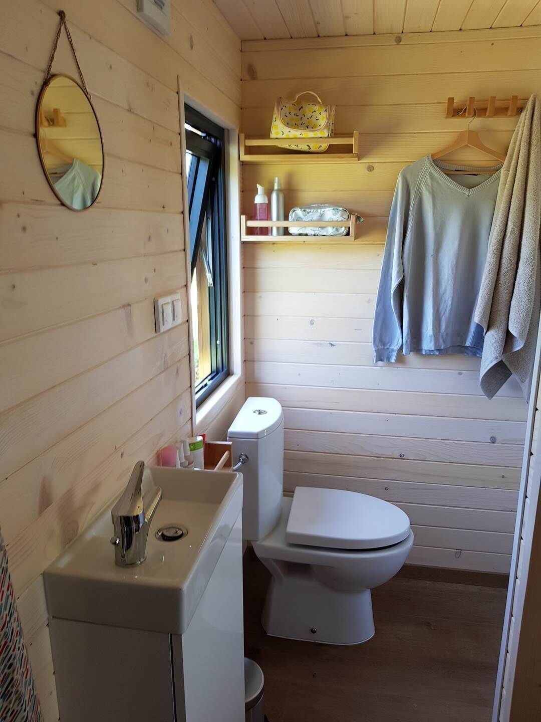 Un baño de cabaña de madera pequeño con inodoro, lavabo y espejo.