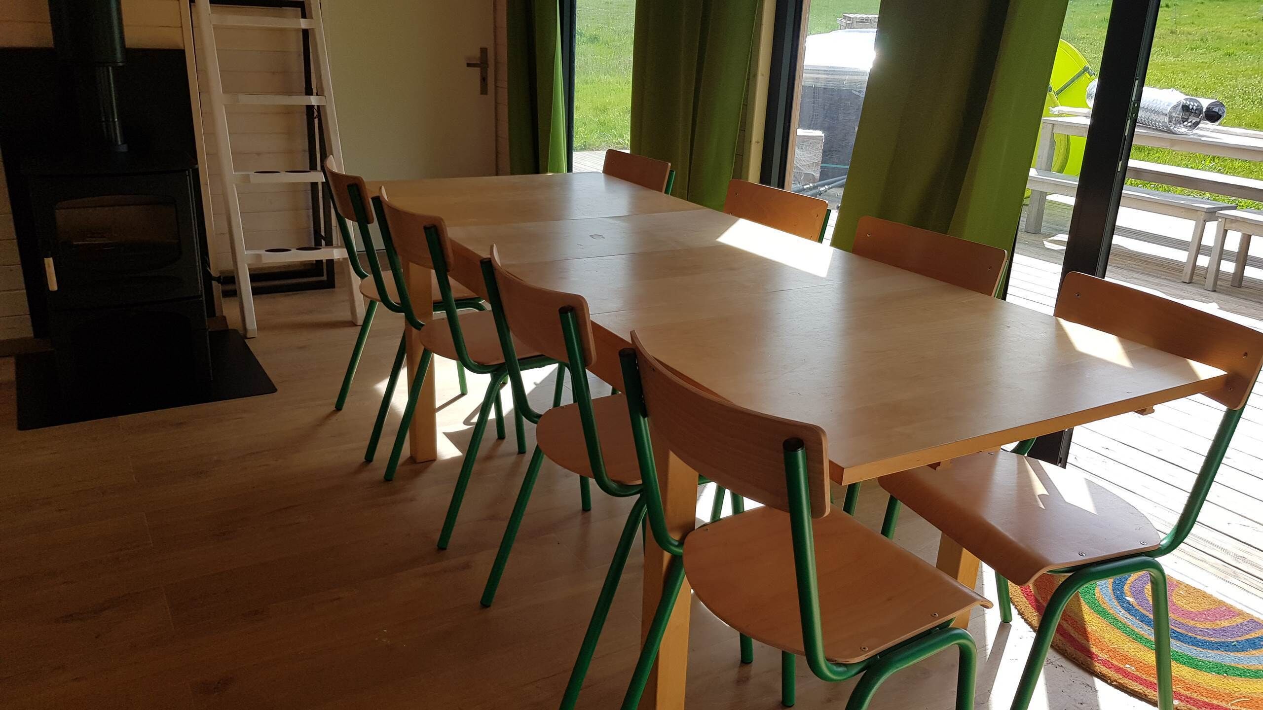 Een kamer met een houten tafel en stoelen, een ladder en uitzicht op de omgeving.
