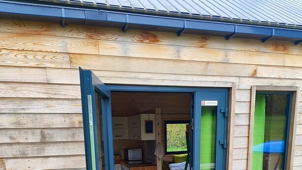 Une cabane en bois, dont la porte est ouverte, laissant entrevoir une cuisine et un espace de vie.