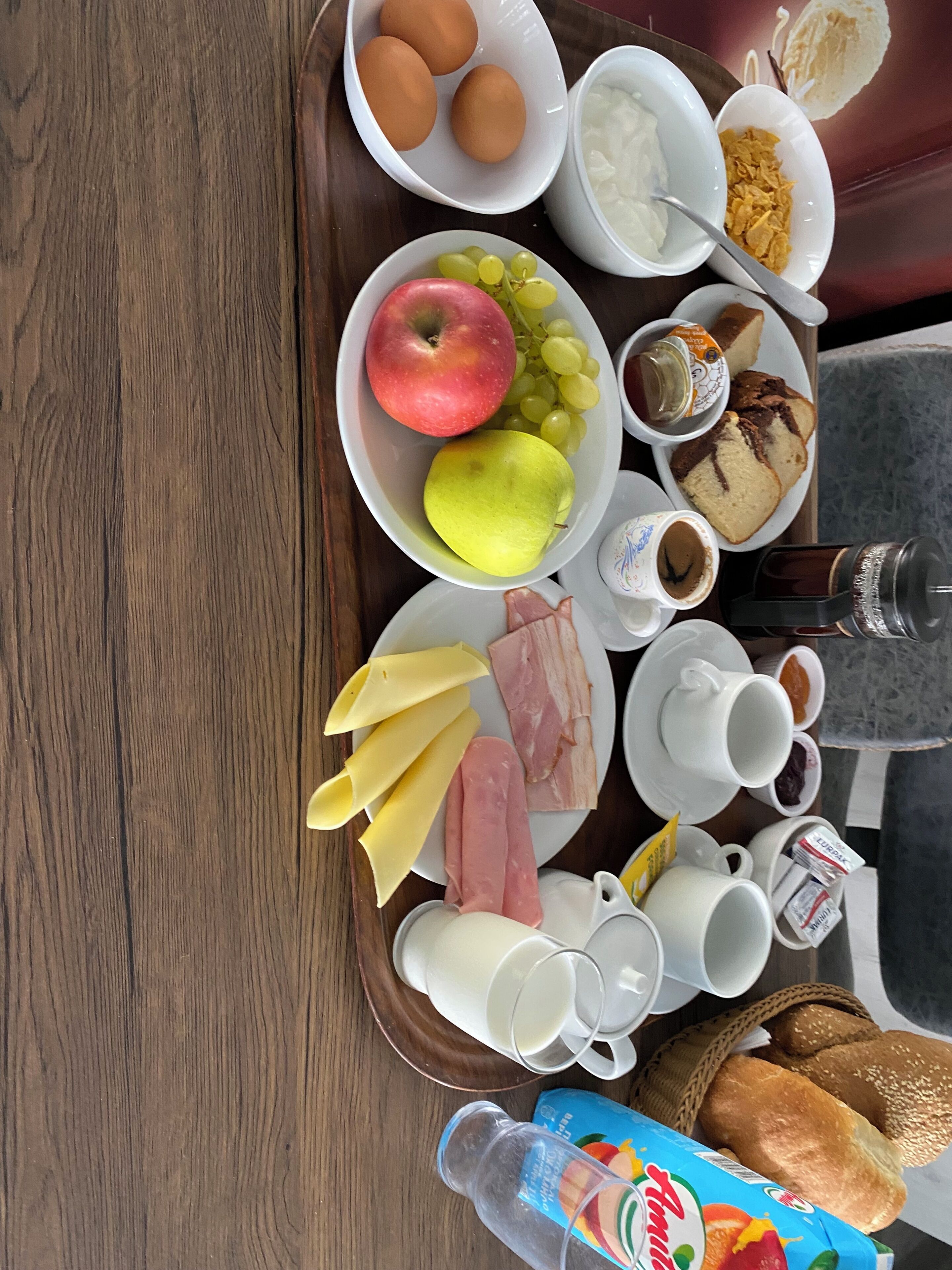 A breakfast tray with eggs, apples, grapes, cheese, ham, bread, and beverages.