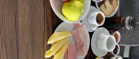 A breakfast tray with eggs, apples, grapes, cheese, ham, bread, and beverages.