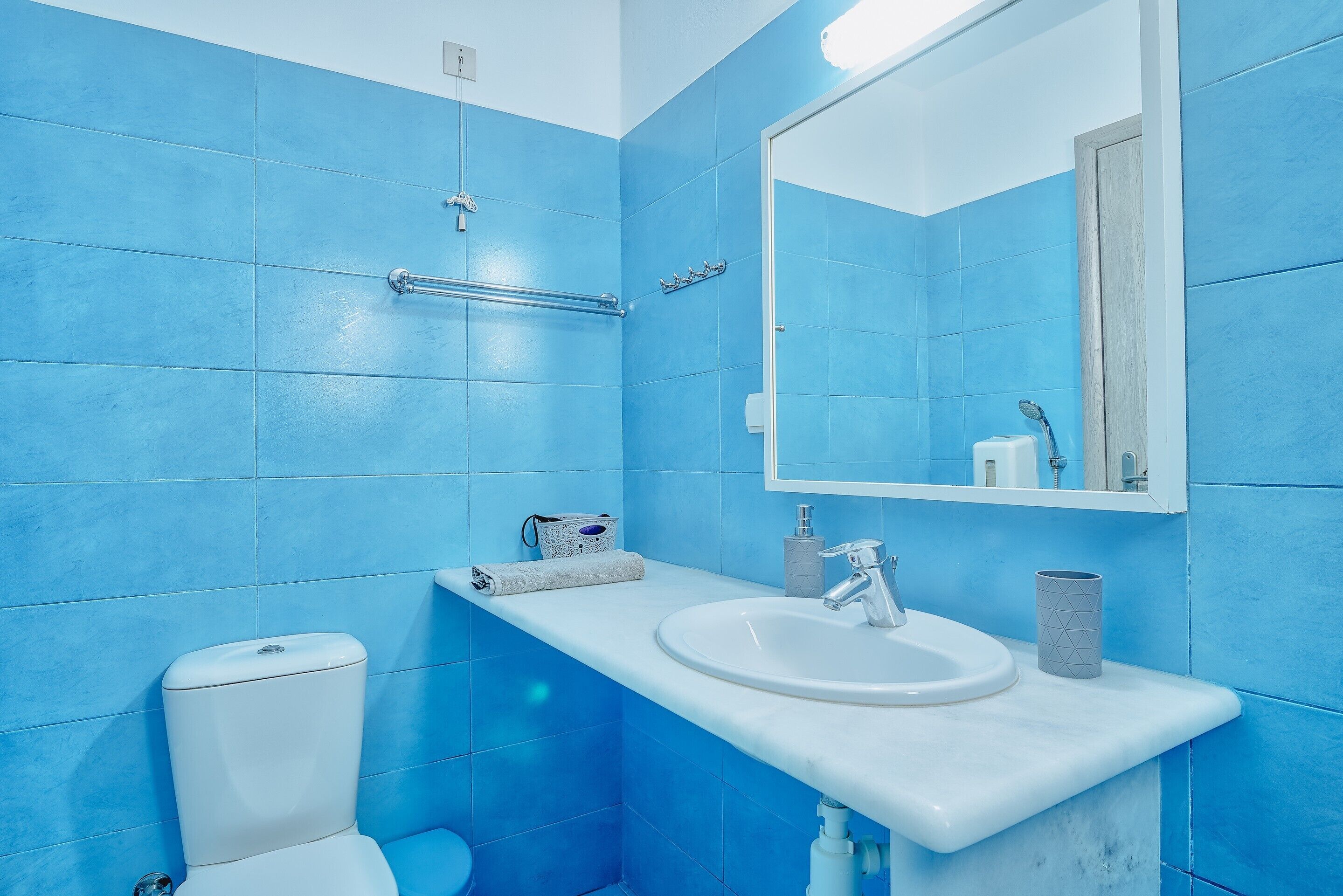 A bathroom with blue tiles, a white sink, a mirror, and a toilet.