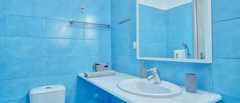 A bathroom with blue tiles, a white sink, a mirror, and a toilet.
