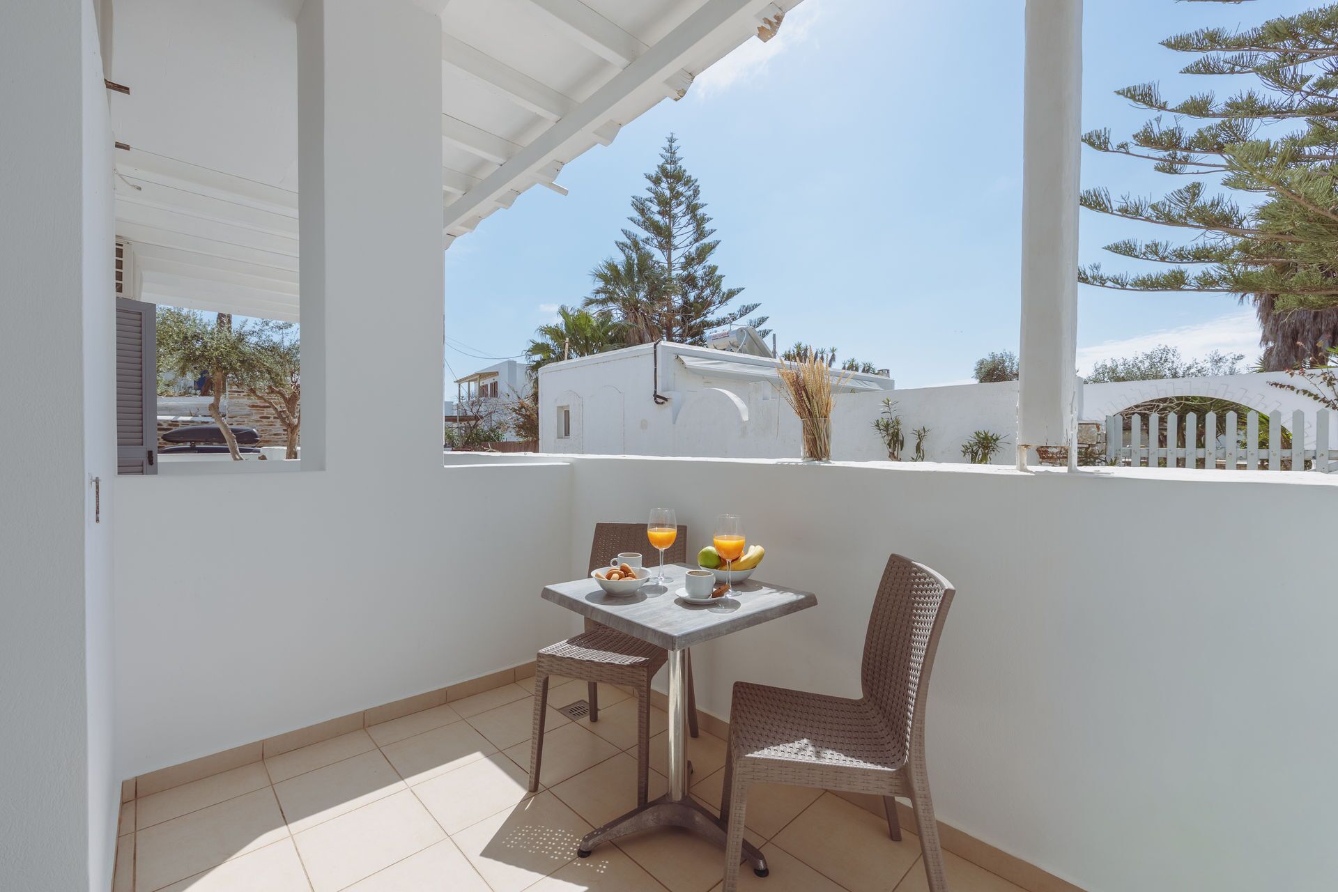 A balcony with a table and chairs, a view of the neighborhood, and a white building in the background.