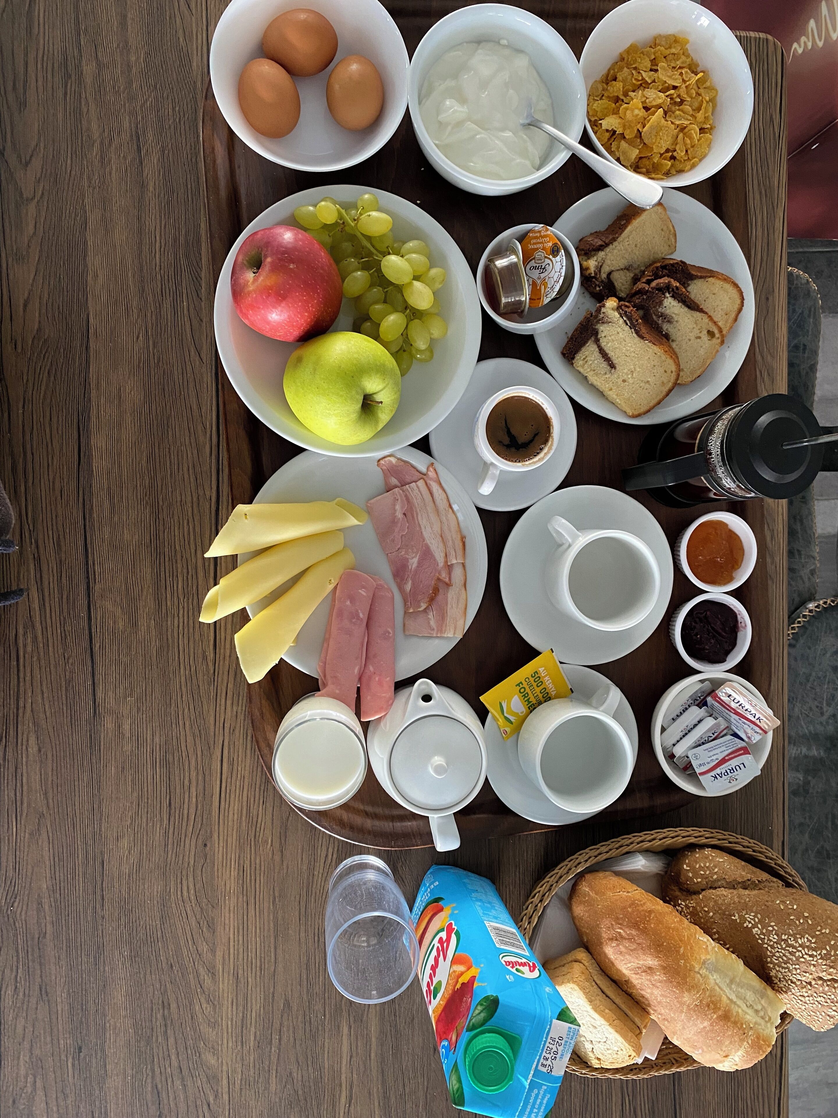 A breakfast tray with eggs, yogurt, cereal, fruits, bread, cheese, ham, coffee, milk, and juice.