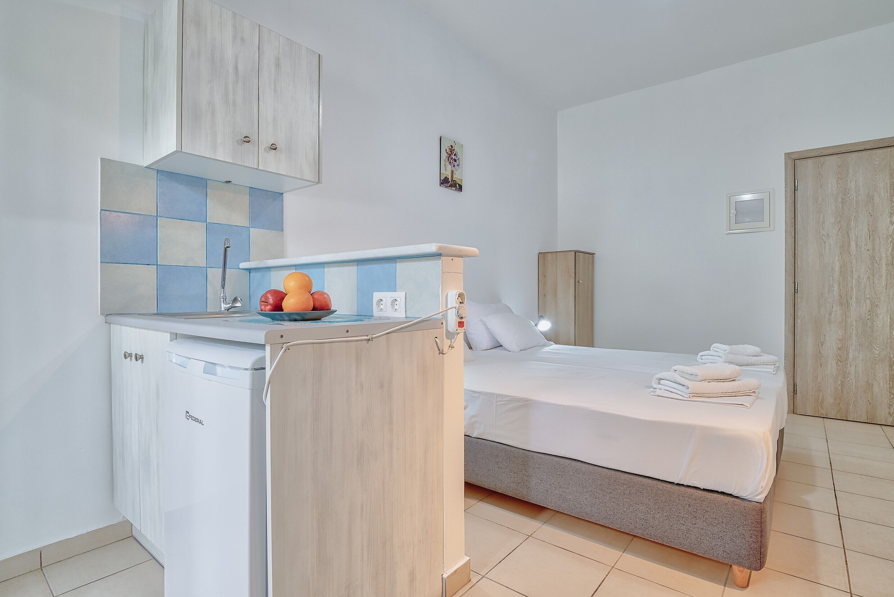 Ein kompaktes Hotelzimmer mit Küchenzeile, einem Bett mit weißer Bettwäsche und einem kleinen Badezimmer.