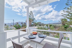 A balcony with a table set for two, overlooking a scenic landscape with trees and buildings. - Pavlos Place (Antiparos)