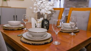 A dining table set with white plates, bowls, and wine glasses, accompanied by a decorative vase with white flowers. - Kijala Suite by Homes By Della (Nairobi)