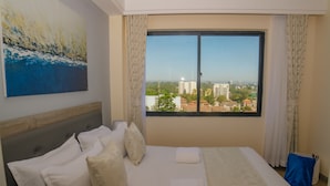 A hotel room with a large bed, a city view through a window, and a painting on the wall. - Kijala Suite by Homes By Della (Nairobi)