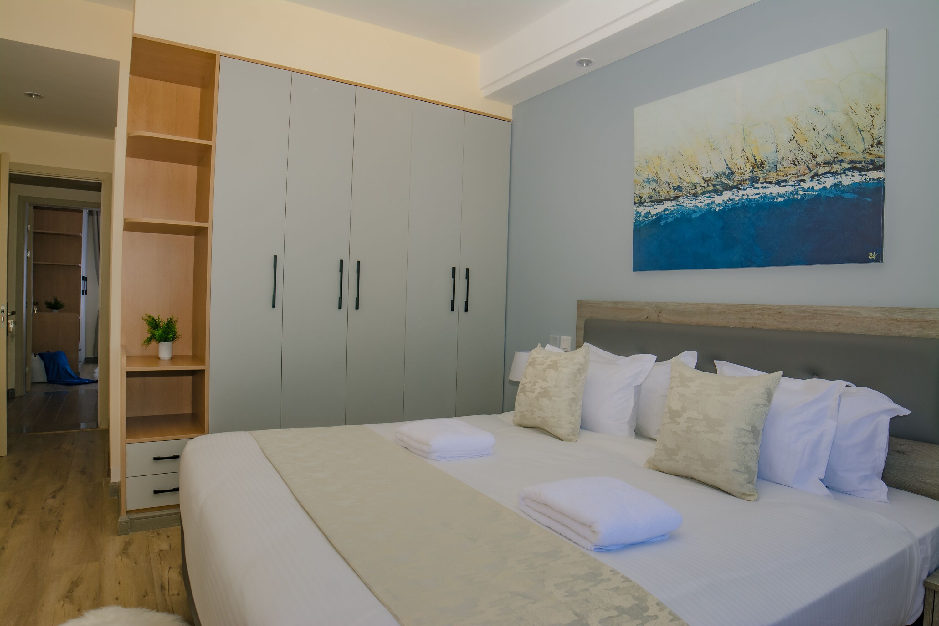 A bedroom with a bed, a wardrobe, a painting, and a small plant.