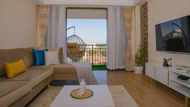 A modern living room with a sofa, a coffee table, a TV, and a balcony with a hanging chair. - Kijala Suite by Homes By Della (Nairobi)