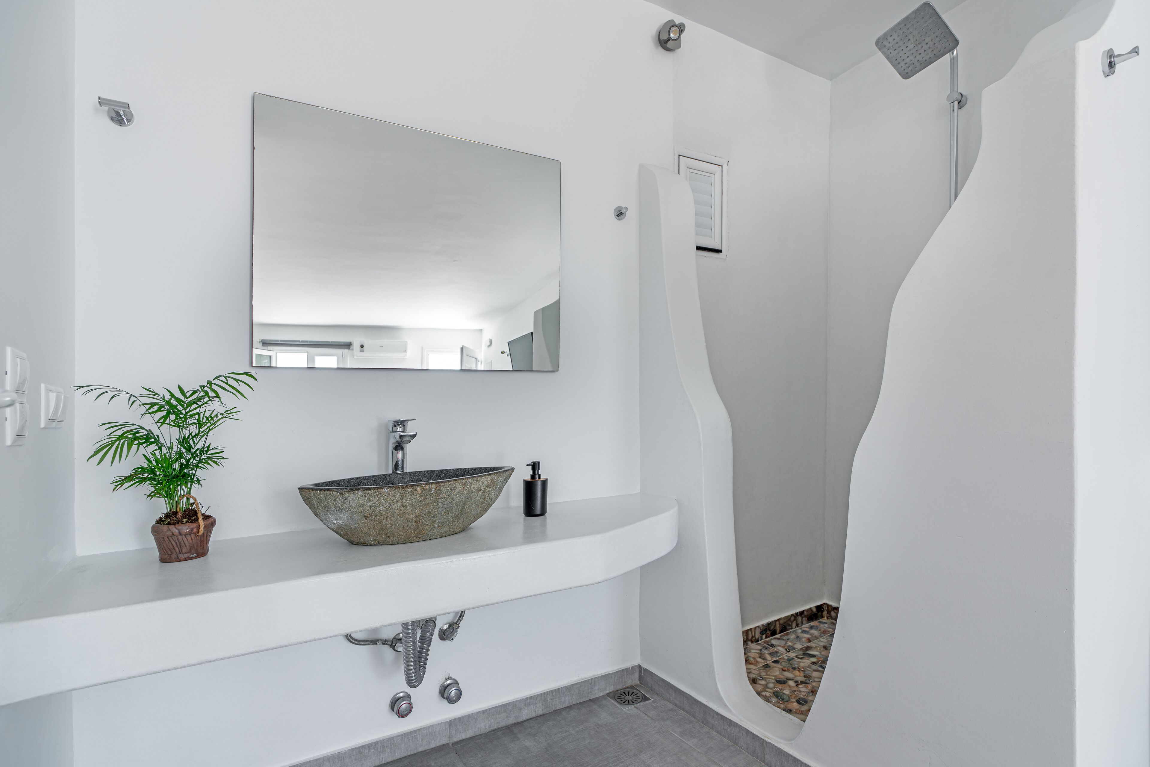 Un baño moderno con un lavamanos blanco, un espejo grande y una ducha con un diseño curvo original.