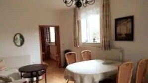 Uma sala de jantar com uma mesa redonda, cadeiras, um lustre e uma janela com cortinas.