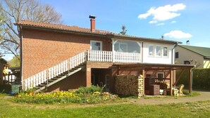 Uma casa de dois andares com fachada de tijolos, uma varanda e um pequeno jardim com flores amarelas.