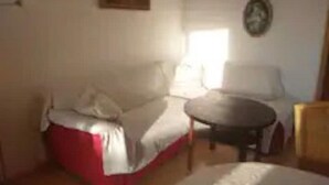 Um quarto com um sofá vermelho e branco, uma mesa redonda pequena e um relógio de parede.