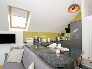 Eine moderne Küche mit Kochinsel, Backofen und Mikrowelle. Ein graues Sofa mit Kissen und ein Flachbildfernseher an der Wand.