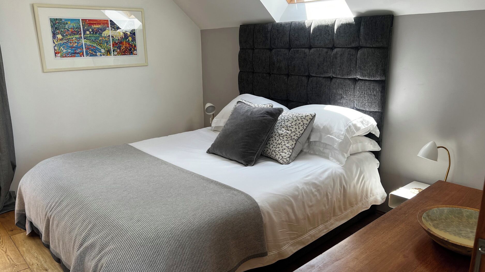 A bedroom with a bed, pillows, a bedside table, a lamp, and a framed picture on the wall.