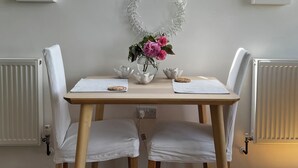 Una mesa de comedor con sillas blancas, un jarrón con flores rosas y un espejo decorativo en la pared.