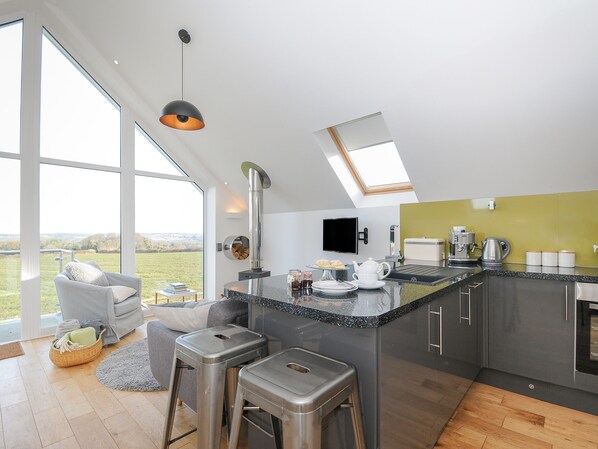 A modern kitchen with a large island, bar stools, a built-in oven, and a TV mounted on the wall.