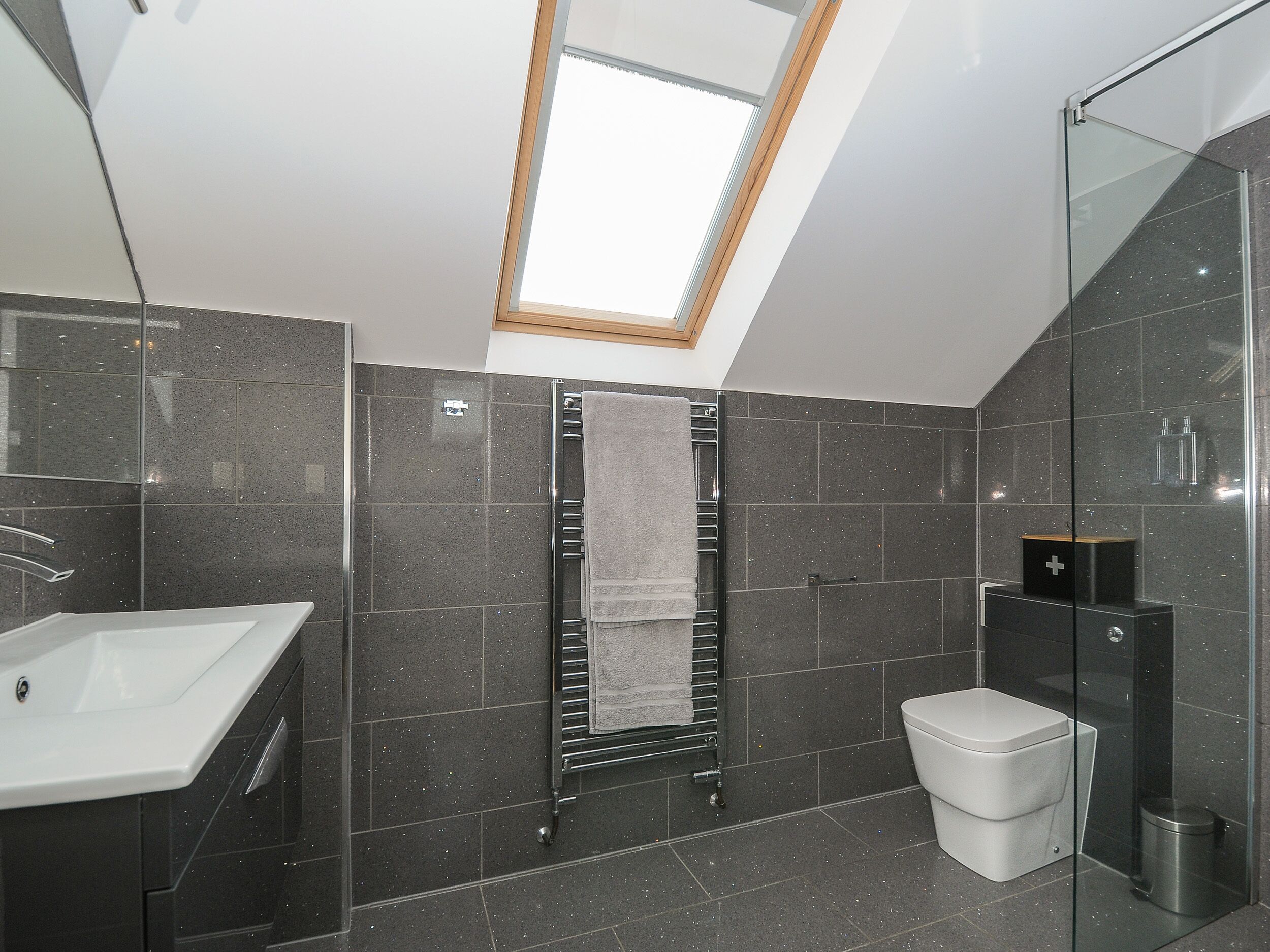 Ein modernes Badezimmer mit Oberlicht, einem weißen Waschbecken, einem Handtuchhalter und einer Toilette.