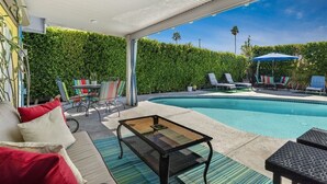 Zona junto a la piscina con un espacio de estar cubierto, sillas de descanso y una mesa.