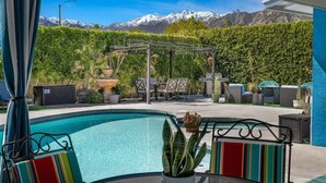 Un área de piscina con sillones reclinables, una pérgola y vistas a montañas nevadas.