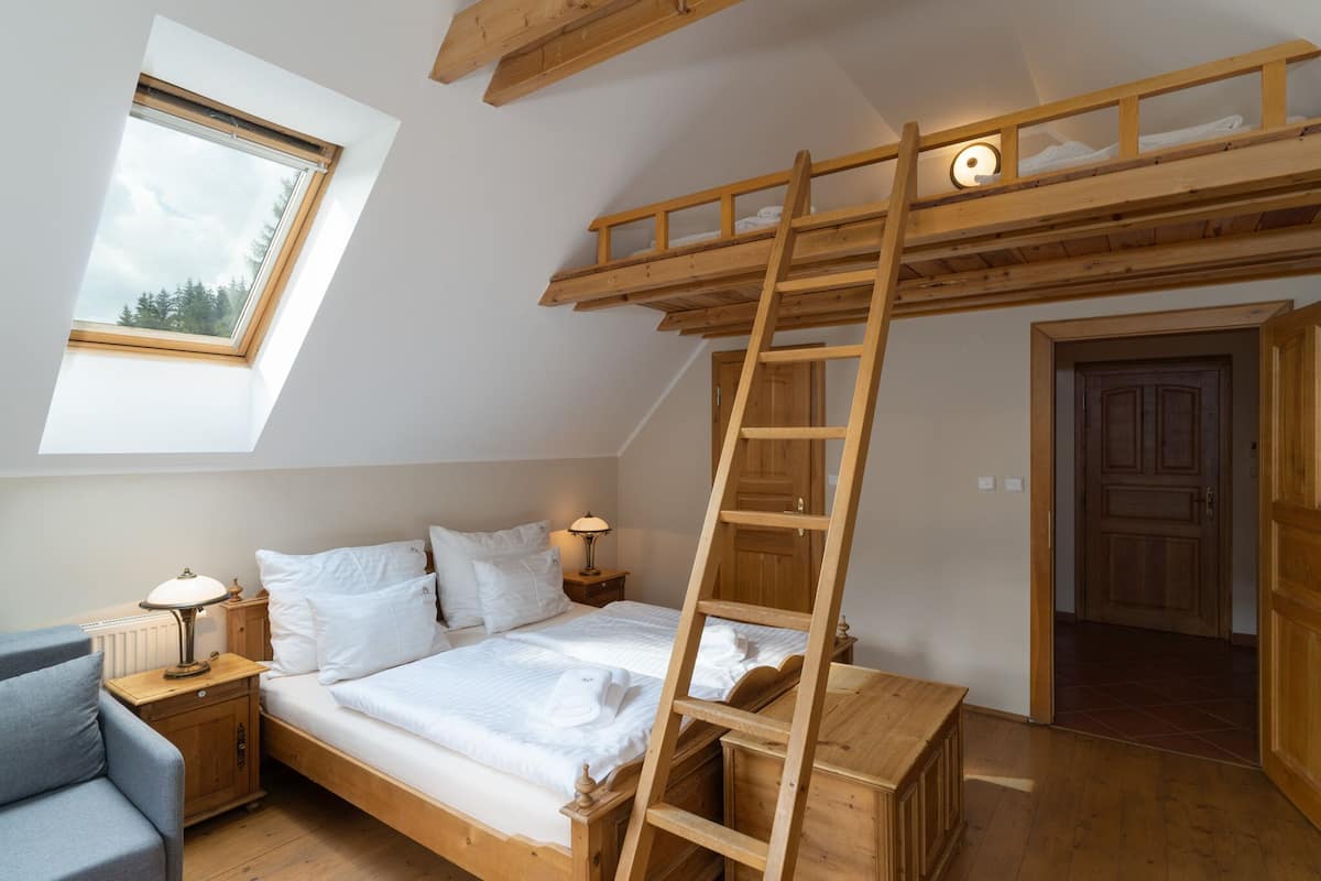 Quarto em estilo loft com beliche de madeira, escada, claraboia, mesa de cabeceira e criado-mudo.