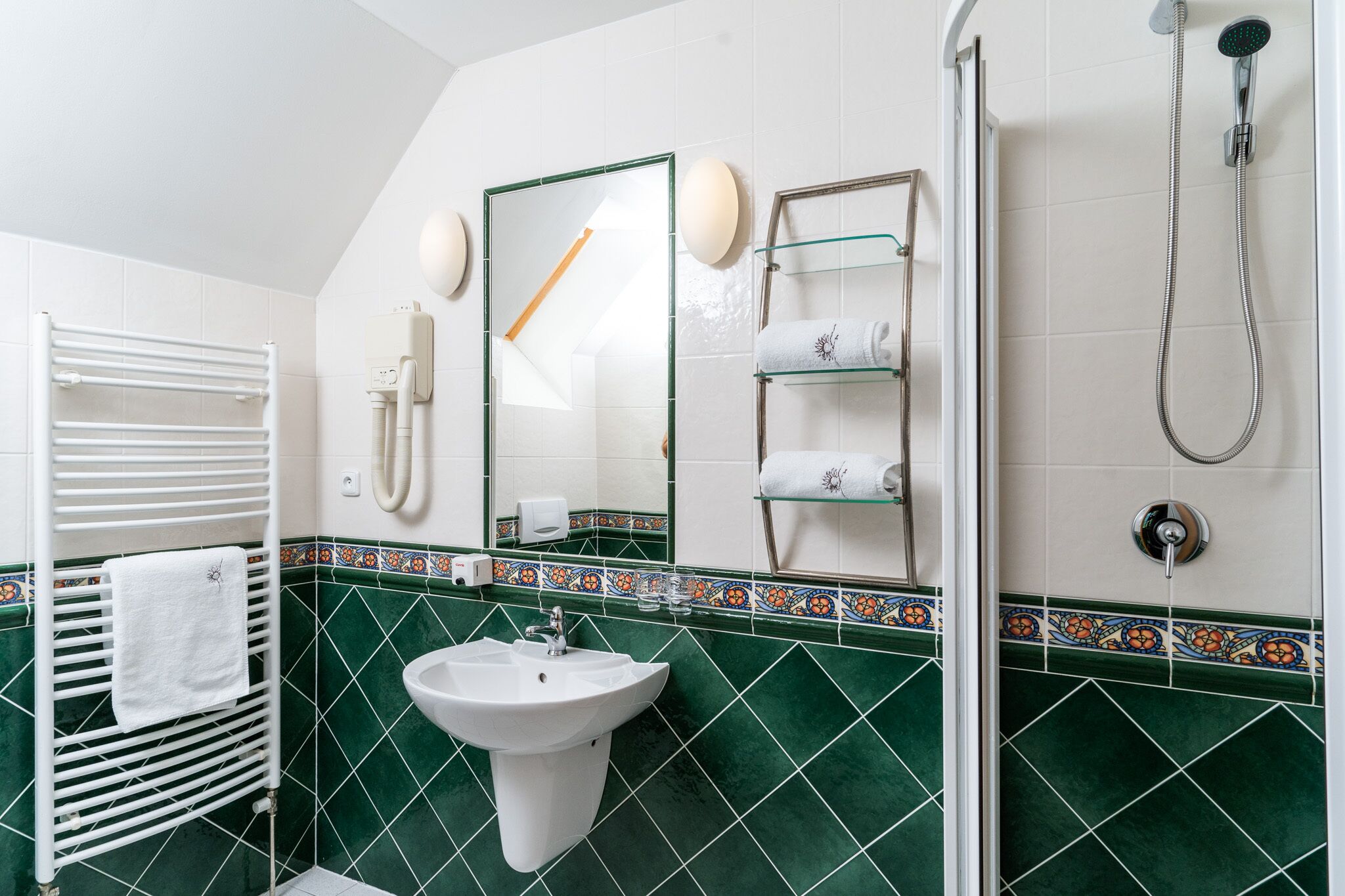 Un baño con lavamanos blanco, cabina de ducha con paredes de vidrio y un perchero con toalla blanca.