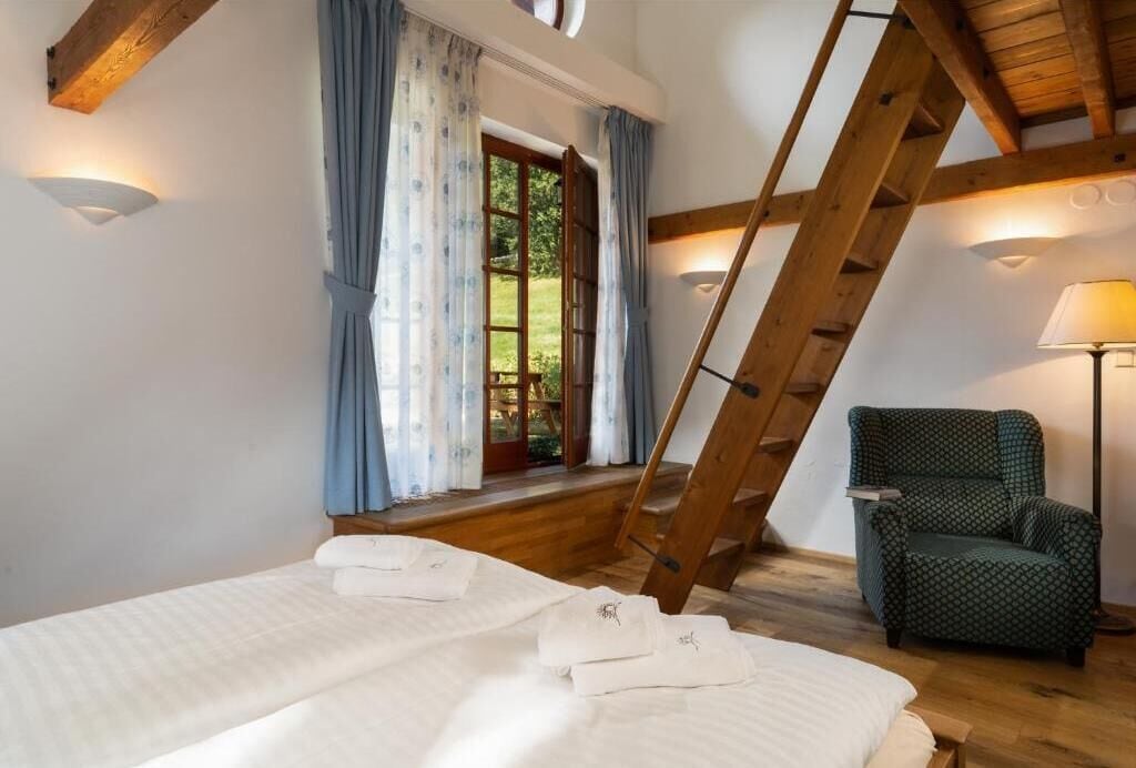 Un dormitorio con una escalera de madera, una silla y una cama con ropa de cama blanca.