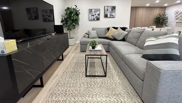 Ein modernes Wohnzimmer mit Fernseher, grauem Sofa und einer schwarzen Unterhaltungsecke.