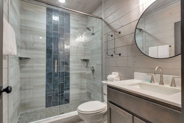 A modern bathroom with a glass-enclosed shower, a white toilet, and a vanity with a sink and mirror.