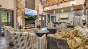 A spacious living area with a stone fireplace, comfortable seating, a large flat-screen TV, and a view of the outdoors.
