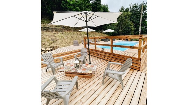 A wooden deck with a pool, outdoor seating, and umbrellas. - . Quiet cottages (Prat-Bonrepaux)