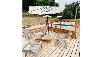Une terrasse en bois avec une piscine, des sièges d’extérieur et des parasols.
