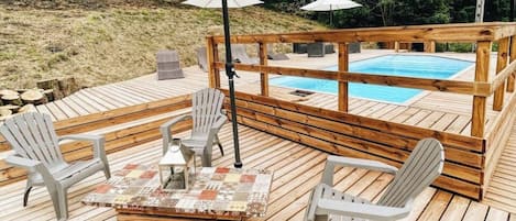 A wooden deck with a pool, outdoor seating, and umbrellas.