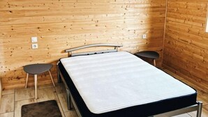 A small, single-bed room with wooden walls, a metal bed frame, a small table, and a chair. - . Quiet cottages (Prat-Bonrepaux)