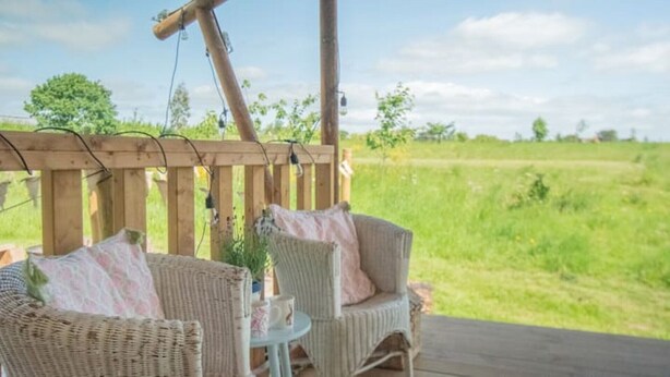 Une terrasse en bois, meublée de meubles en osier, avec vue sur un champ verdoyant.