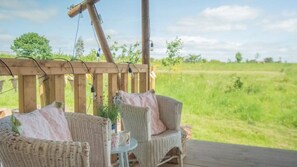 Eine Holzterrasse mit Korbmöbeln und Blick auf ein Grasfeld.
