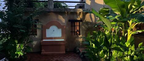 A courtyard with a brick pathway, a white bench, and lush green plants.