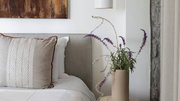 A bedroom with a bed, pillows, a bedside table with a plant, a wall-mounted light, and a large abstract painting.